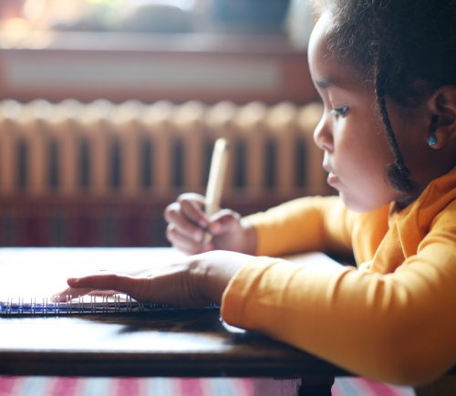 Profile of little African girl writing  in classroom.